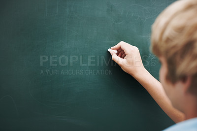 Buy stock photo Rear view of a young boy writing something on a blackboard with a piece of chalk - copyspace