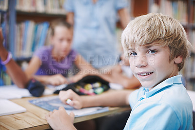 Buy stock photo A young boy looking over his shoulder while in the library with his peers