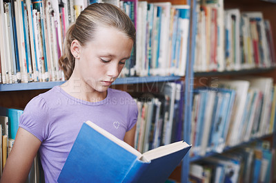 Buy stock photo A cute young girl engrossed in a book in the library