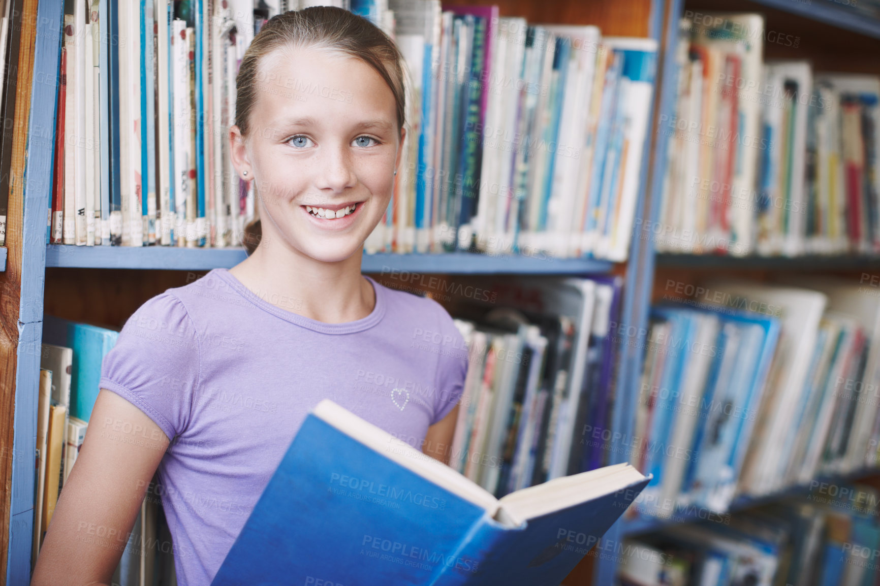 Buy stock photo Portrait of a cute young girl engrossed in a book in the library