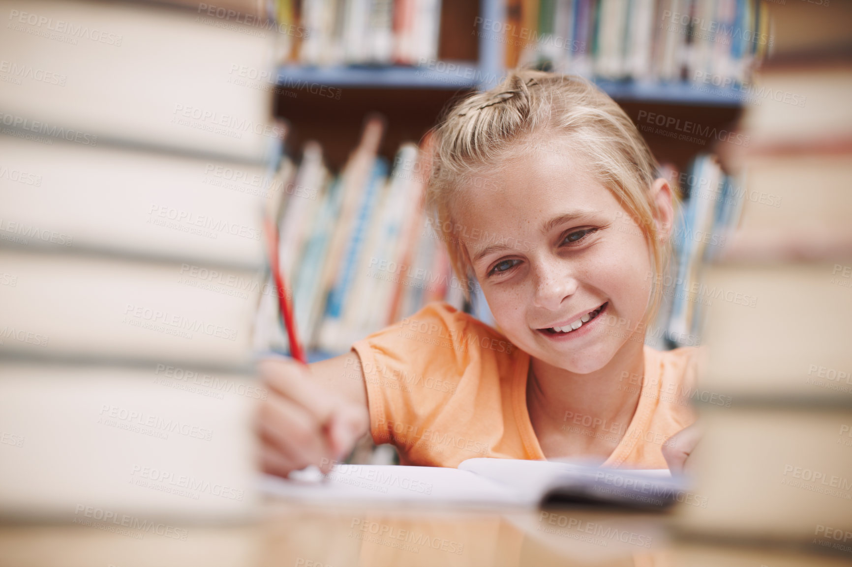 Buy stock photo Child, writing and smile in library for education, knowledge and happy for development at elementary school. Young girl, learning and books on table for fun lesson, growth and progress in assessment