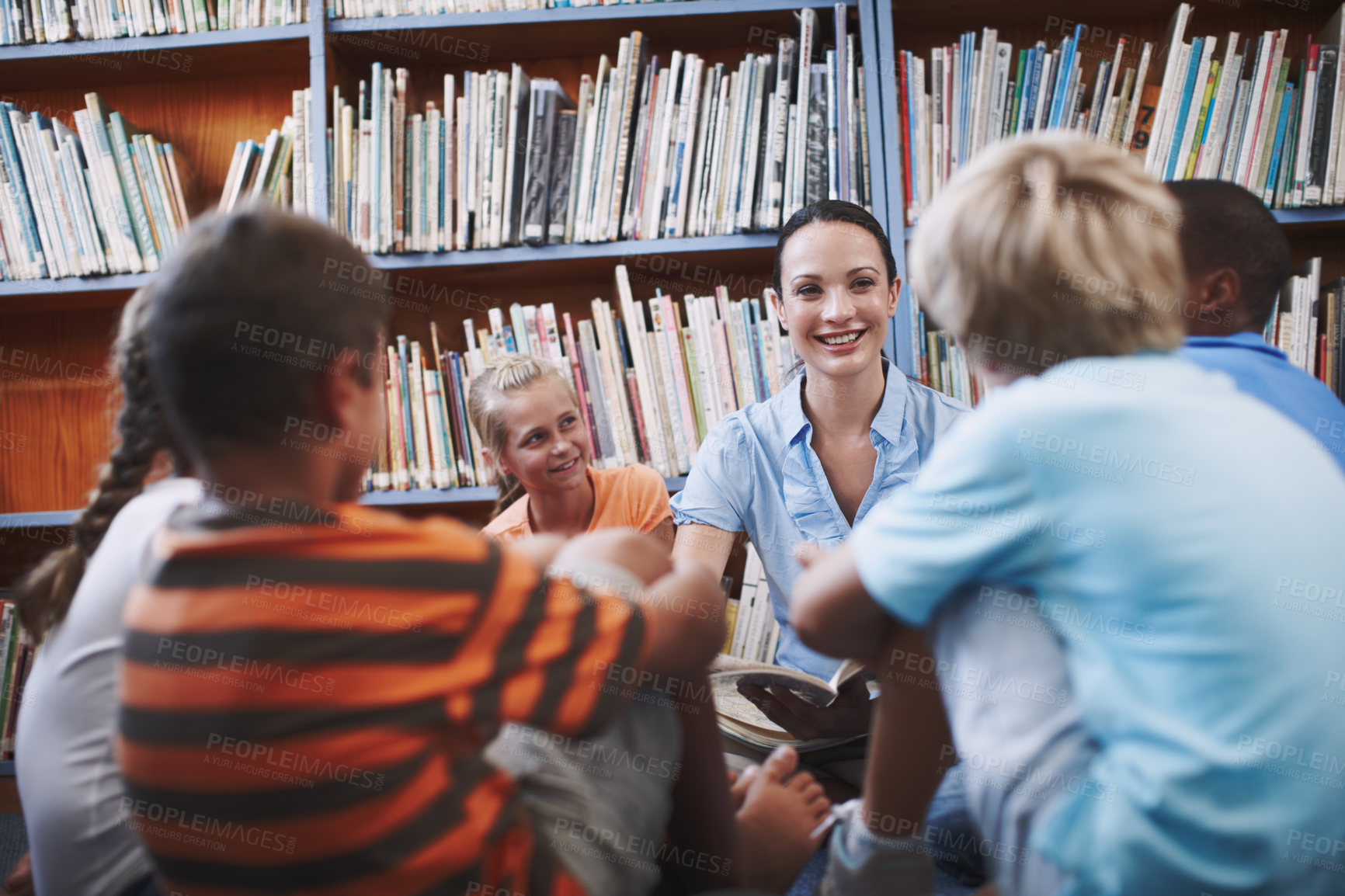 Buy stock photo A pretty teacher sitting with her excited students in the library