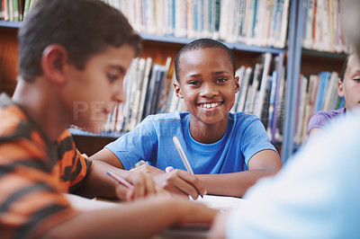 Buy stock photo An african american boy sitting in the library and working with his classmates