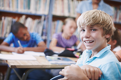Buy stock photo An excited young boy sitting in the library with his classmates