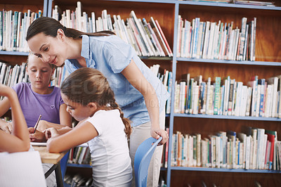 Buy stock photo A pretty young teacher helping her students with their work in the library