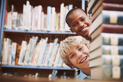 Buy stock photo Two school friends peering around a stack of books in the library