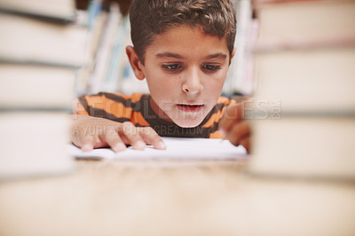Buy stock photo A cute young boy doing schoolwork while surrounded by books at the library