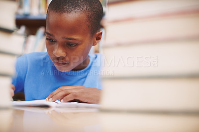 Buy stock photo A cute young boy writing a story in the library while surrounded by books