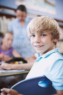 Buy stock photo An excited young boy sitting in the library with his classmates