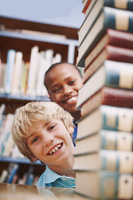 Buy stock photo Boys, portrait and books in library for education, learning and fun with hiding, knowledge and info. Student, face and playing in school for development, study and history with academic scholarship