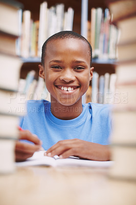 Buy stock photo An african american boy smiling at you in the library between a stack of books