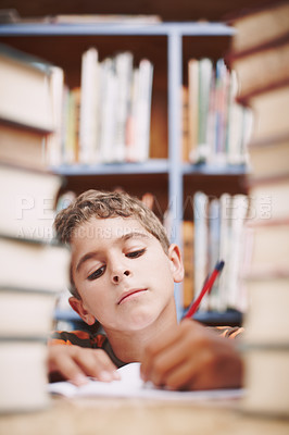 Buy stock photo A young boy doing some creative writing between a stack of books