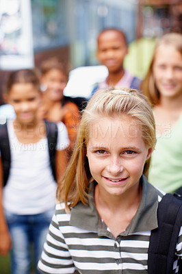 Buy stock photo Sweet schoolgirl smiling up at the camera with friends in the background - copyspace
