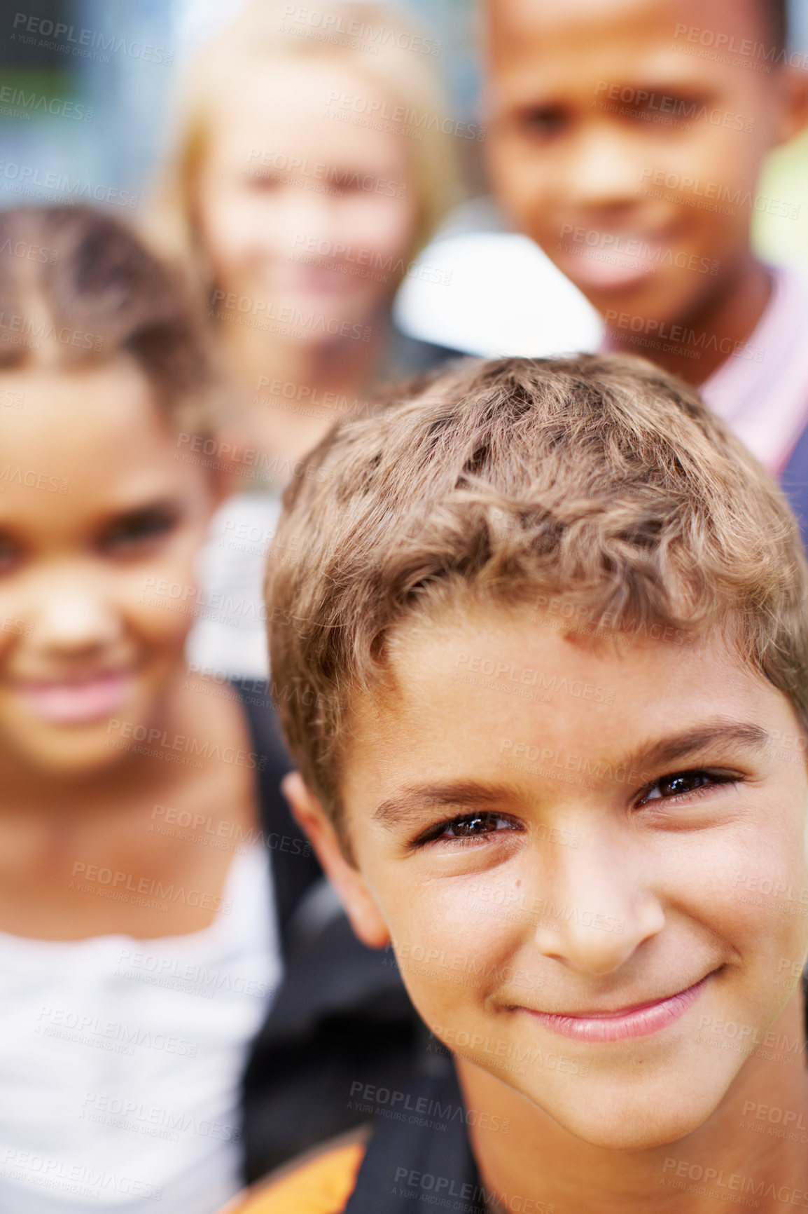 Buy stock photo Handsome boy smiling up at the camera with his school friends behind him