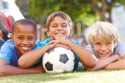 Buy stock photo Three happy boys lying outside in the sun with their soccerball - copyspace