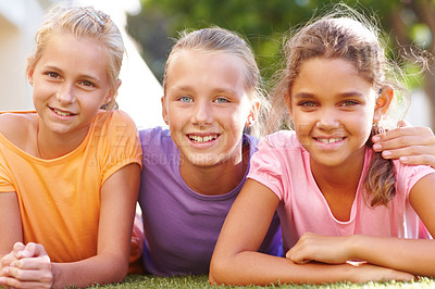 Buy stock photo Portrait of three girls lying on the grass on a sunny afternoon smiling at you