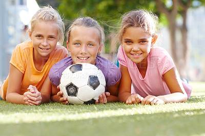 Buy stock photo Three smiling girls lying on some sunny grass posing with a soccer ball- copyspace