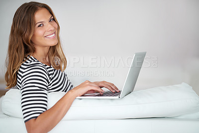 Buy stock photo Portrait of a young woman using a laptop while sitting on a sofa at home