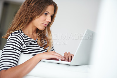 Buy stock photo Shot of a young woman using a laptop while sitting on a sofa at home
