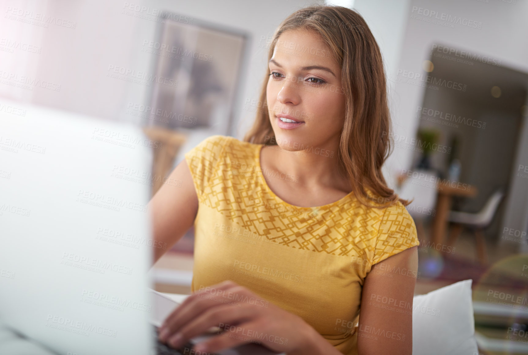 Buy stock photo Shot of a young woman using a laptop while sitting on a sofa at home