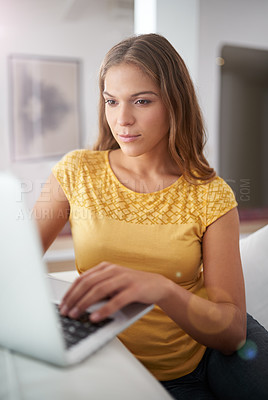 Buy stock photo Shot of a young woman using a laptop while sitting on a sofa at home