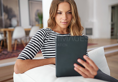Buy stock photo Shot of a young woman using a digital tablet while sitting on a sofa at home