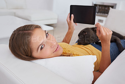 Buy stock photo Portrait of a young woman using a digital tablet while lying on a sofa with her dog
