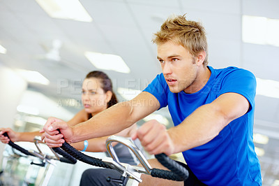 Buy stock photo Young man cycling at the gym with woman in background