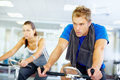 Buy stock photo Young man training on exercise bike with woman in background