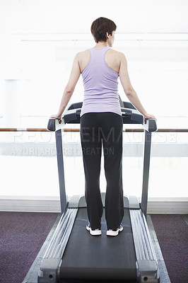 Buy stock photo Rearview shot of a young woman standing on the treadmill at the gym