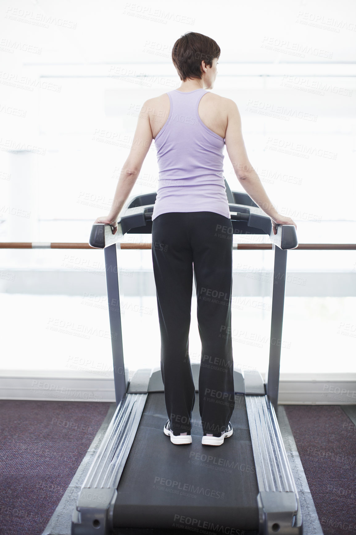 Buy stock photo Rearview shot of a young woman standing on the treadmill at the gym