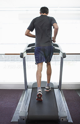 Buy stock photo Rearview shot of a young man running on the treadmill at the gym