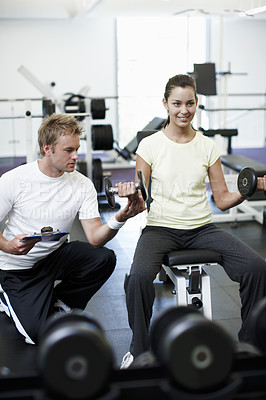 Buy stock photo Cropped shot of an attractive young woman weight training with her personal trainer