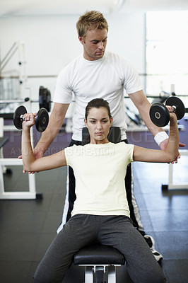 Buy stock photo Cropped shot of an attractive young woman weight training with her personal trainer