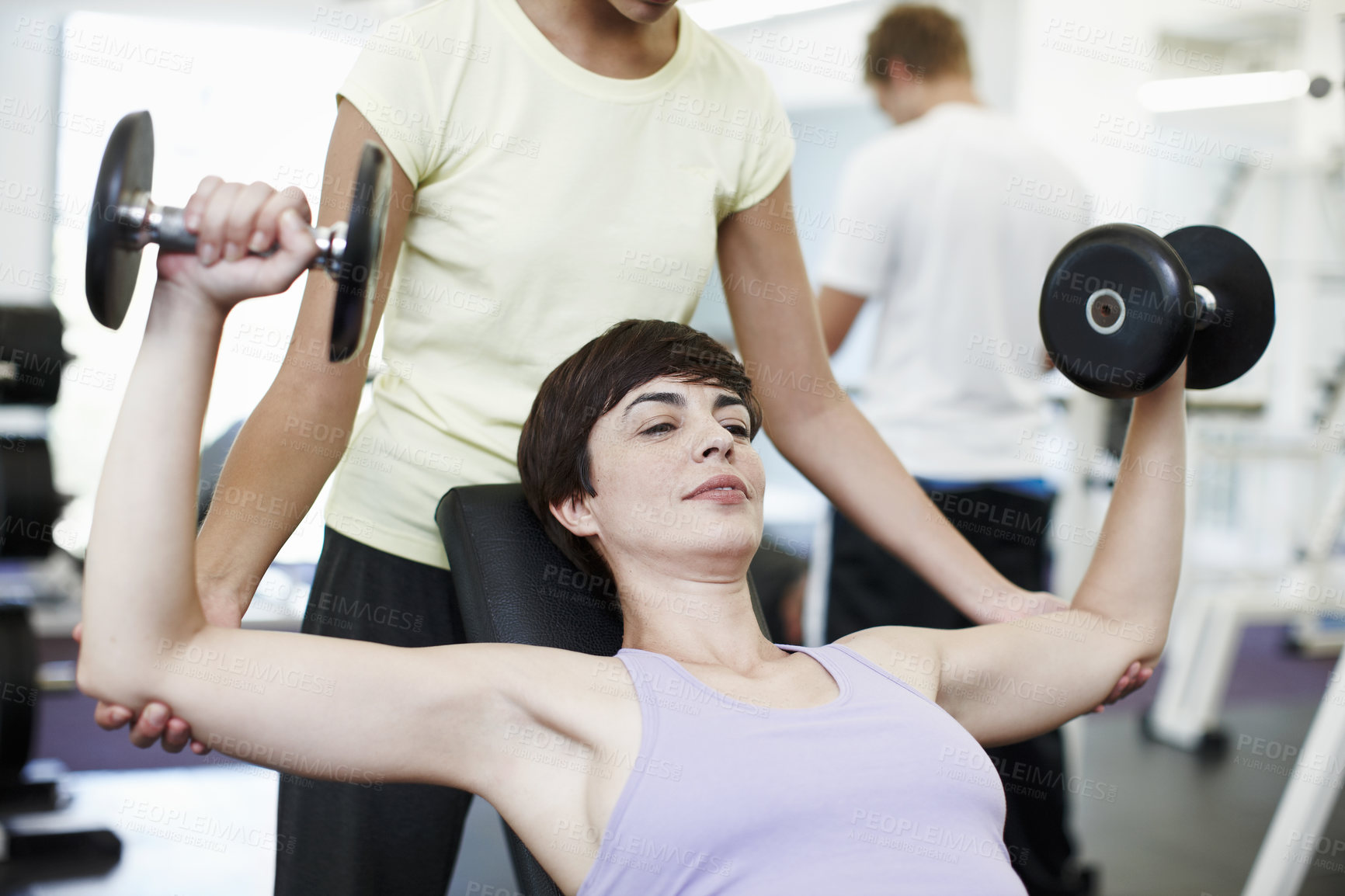 Buy stock photo Cropped shot of an attractive young woman training on the weights with her personal trainer