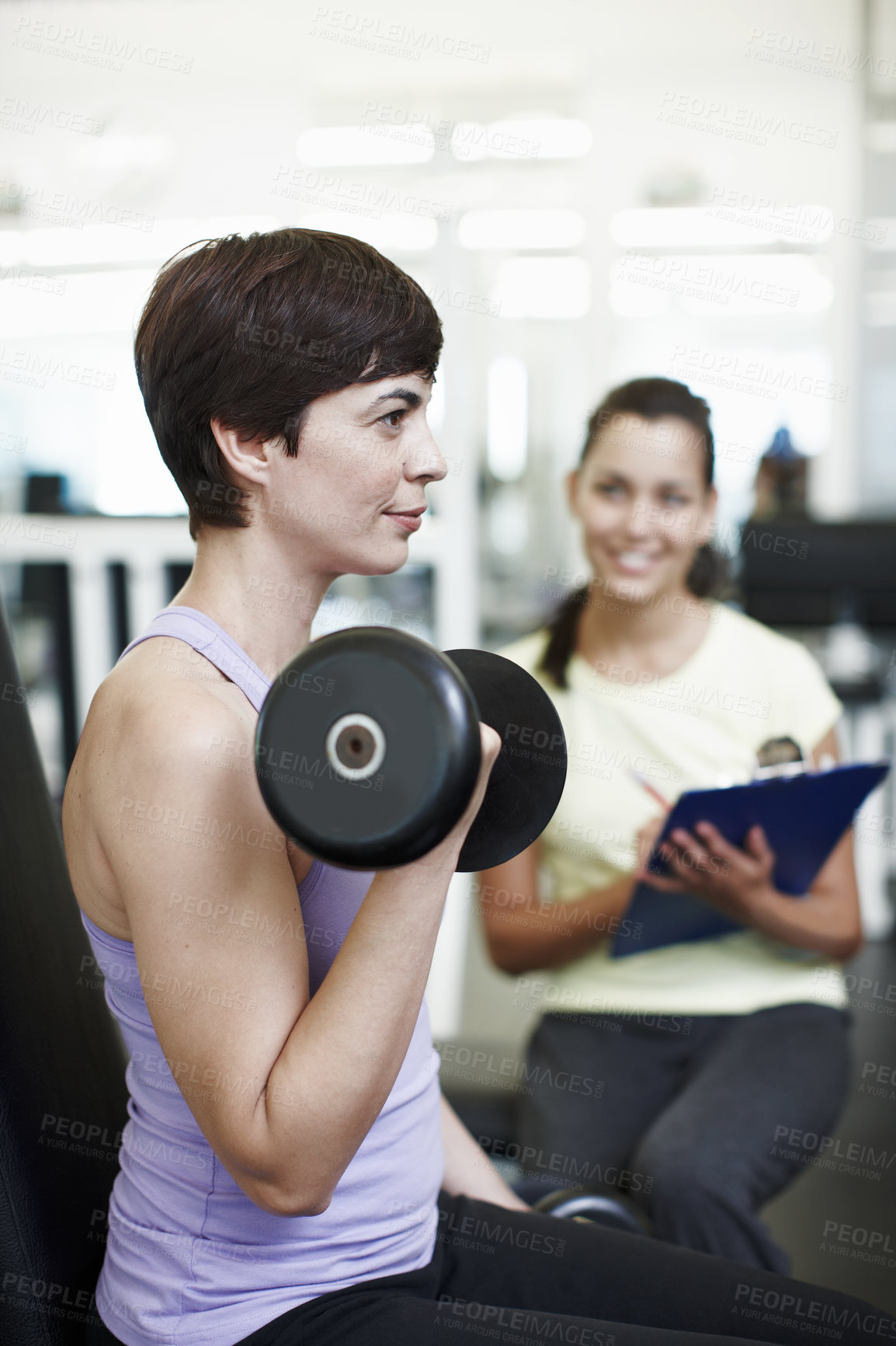 Buy stock photo Cropped shot of an attractive young woman training on the weights with her personal trainer