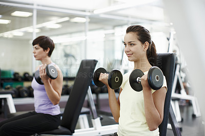 Buy stock photo Cropped shot of two young women working with dumbbells in the gym