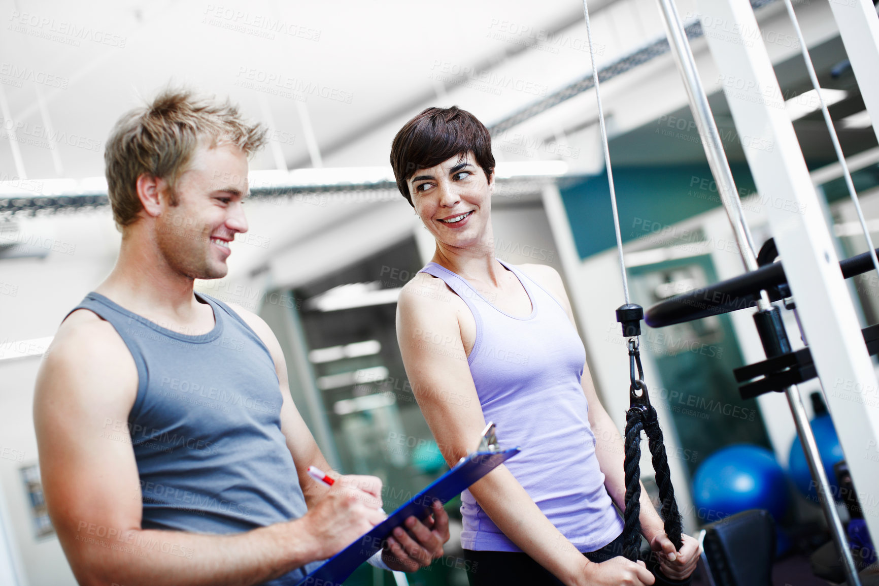 Buy stock photo Cropped shot of an attractive young woman exercising in the gym while her personal trainer takes notes