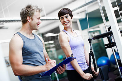 Buy stock photo Cropped shot of an attractive young woman exercising in the gym while her personal trainer takes notes