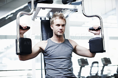 Buy stock photo Cropped shot of a handsome young man using an exercise machine in the gym