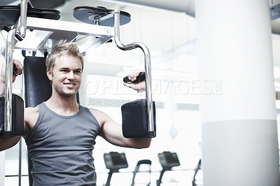 Buy stock photo Cropped shot of a handsome young man using an exercise machine in the gym