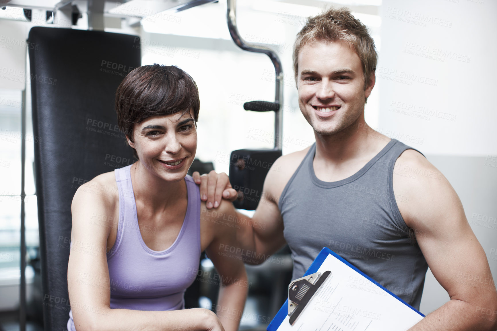 Buy stock photo Personal trainer, woman and clipboard by machine in portrait, smile or progress for weightlifting at gym. People, man and coach with checklist for happy, help or exercise with notes at club in Greece