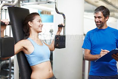 Buy stock photo Cropped shot of an attractive young woman using an exercise machine while her personal trainer looks on