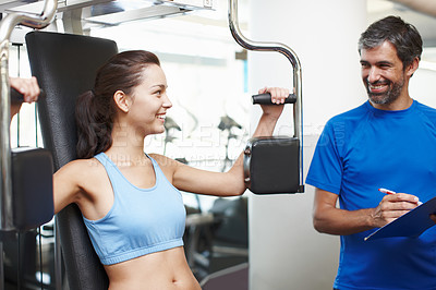 Buy stock photo Cropped shot of an attractive young woman using an exercise machine while her personal trainer looks on