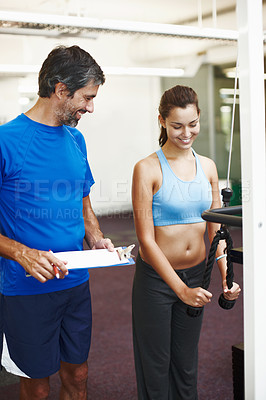 Buy stock photo Cropped shot of an attractive young woman exercising in the gym while her personal trainer takes notes