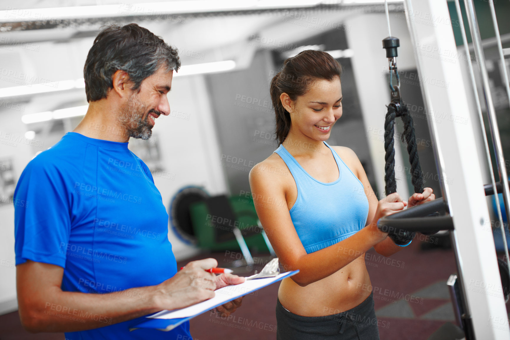 Buy stock photo Cropped shot of an attractive young woman exercising in the gym while her personal trainer takes notes