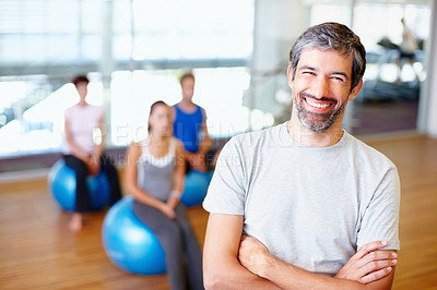 Buy stock photo Portrait of smiling male gym trainer with people practicing yoga in background