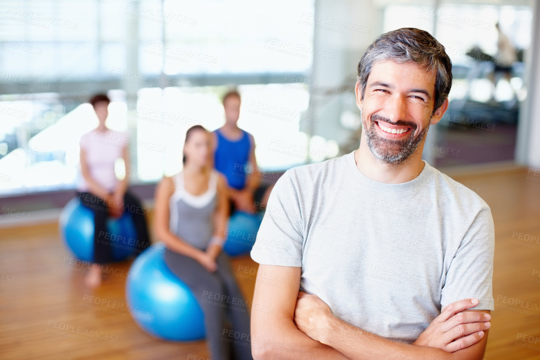 Buy stock photo Portrait of smiling male gym trainer with people practicing yoga in background