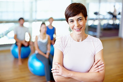 Buy stock photo Portrait of smiling female gym trainer with people practicing yoga in background