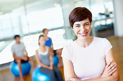 Buy stock photo Portrait of beautiful female gym trainer with people practicing yoga in background
